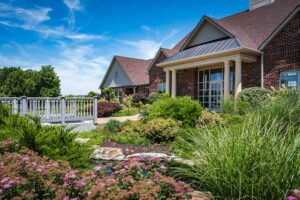 A bridge going over a stream to leasing office at The Waterways of Lake Saint Louis, surrounded by beautiful landscaped grounds.