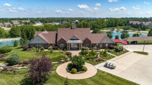 Exterior view of the clubhouse at The Waterways of Lake Saint Louis near a pond with beautifully landscaped grounds.