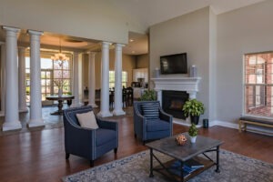 A lounge area with seating, an indoor fireplace, and columns surrounding an entryway in a clubhouse.
