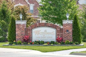 Exterior brick entry sign for The Waterways of Lake Saint Louis Luxury Apartment Homes with two lanterns surrounded by manicured landscaping.