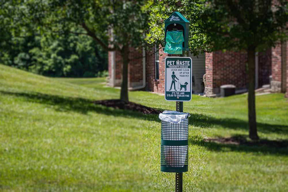 A pet waste station with disposable bags in a large grassy area at the pet-friendly apartment community of The Waterways at Lake Saint Louis.