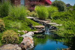 A cascading waterfall going into a pond surrounded by lush greenery at The Waterways of Lake Saint Louis