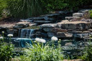 Water cascading into a small pond surrounded by flowers and plants at The Waterways at Lake Saint Louis.