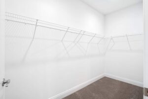 A large walk-in closet with plush carpet, baseboards, and a wrap-around shelf for hanging clothes.