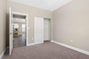 A secondary bedroom with a closet, plush carpeting, and access to the kitchen and living room.