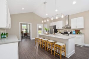 A spacious kitchen with hanging pendant lights, an island bar, and access to a nearby office space and private patio.