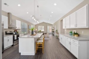 A large kitchen space with pendant lighting, stainless steel appliances, and an island bar flowing into the living room.