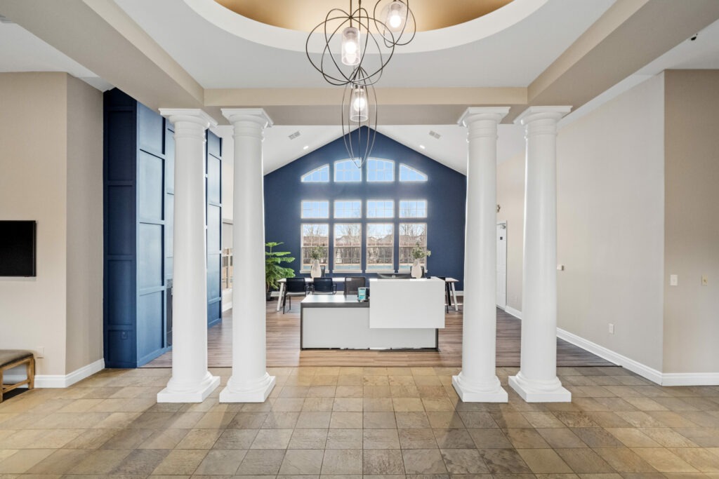 The Waterways of Lake Saint Louis' reception area with 4 large pillars near a fireplace lounge and a collaborative workspace.